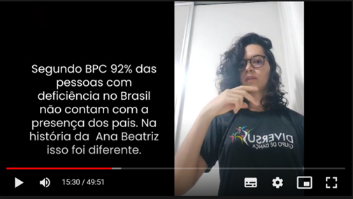 Em fundo preto, com letras brancas, está
escrito: “Segundo pesquisas do BPC, 92% das pessoas com deficiência no
Brasil não contam com a presença dos pais. Com a Ana Beatriz, isso foi
diferente”. À direita, intérprete de Libras, de cabelo preto, óculos,
vestindo camiseta preta com logo do Grupo de Dança Diversus.